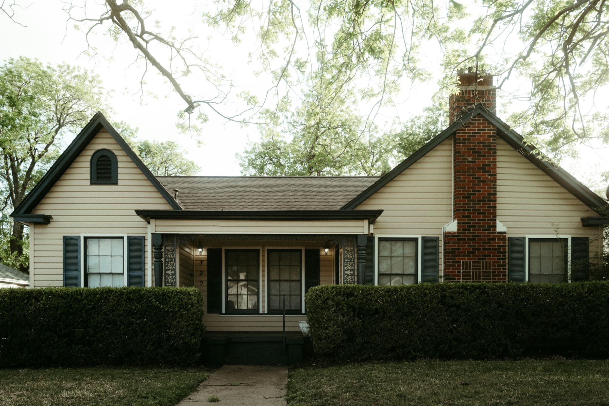 Outdated house facade with old siding and overgrown hedges